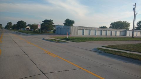 A row of grey self-storage units situated beside a paved road under a clear, bright sky.