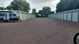 A gravel path between two rows of white self-storage units, with a recreational vehicle parked on the left.