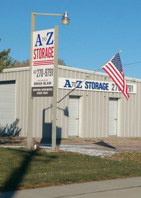 A silver metal A-to-Z Storage building with a large vertical sign and an American flag on a sunny day.