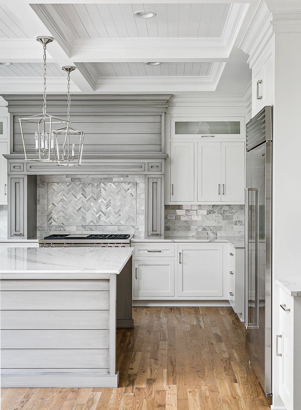 A kitchen with white cabinets , stainless steel appliances , hardwood floors and a large island.