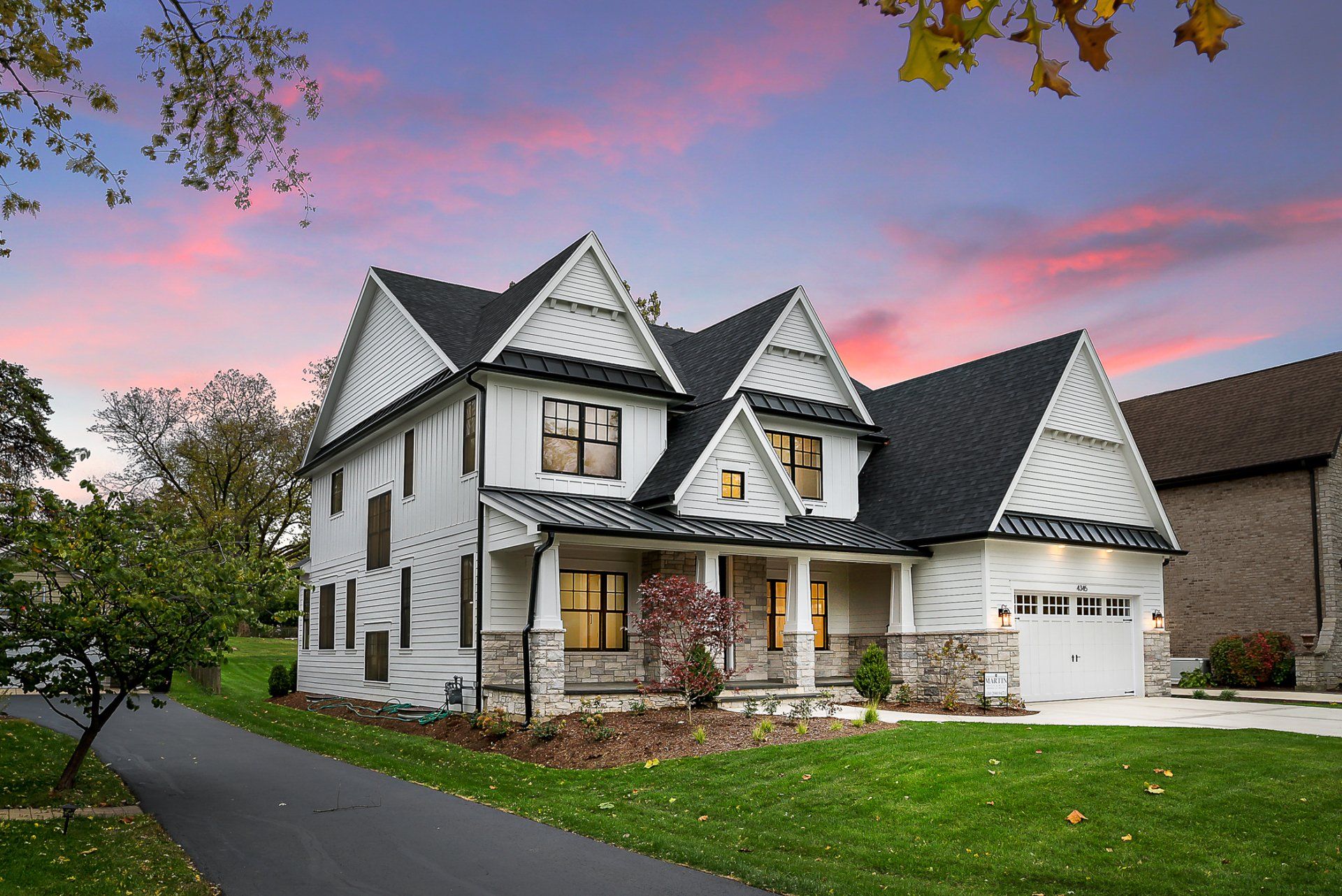 A large white house with a black roof is sitting on top of a lush green field.