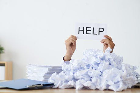 hands holding up a help sign underneath stack of papers
