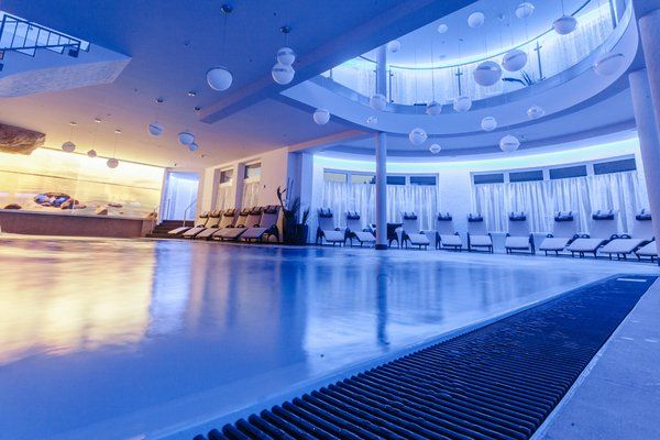 Hallenbad mit Liegestühlen, weißen Kugeln, die von der Decke hängen, blauer Beleuchtung.