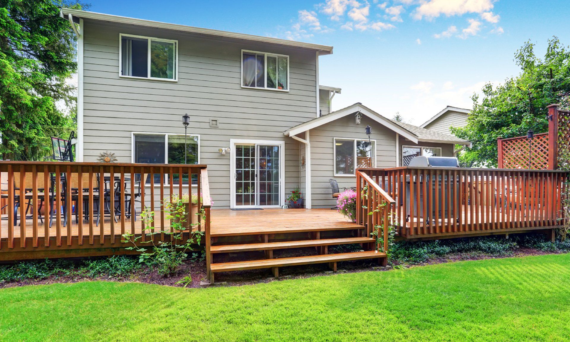 Jardin avec terrasse en bois, maison et pelouse verte par une journée ensoleillée.