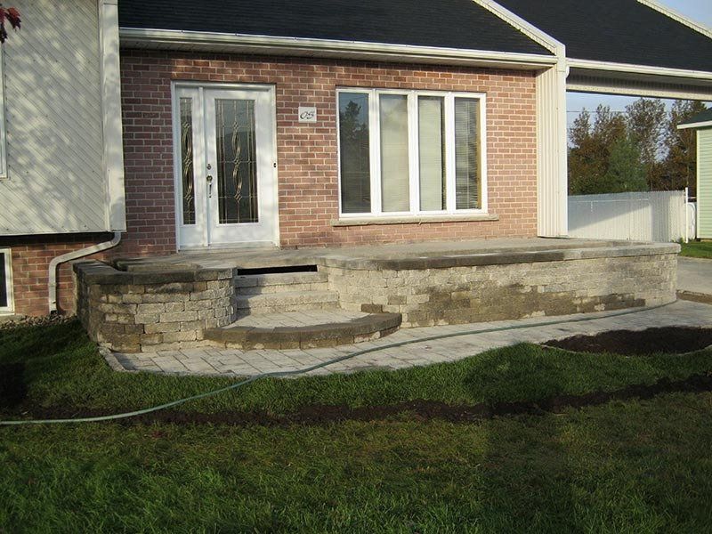 Maison en briques avec porche et marches en béton. Allée pavée. Pelouse.