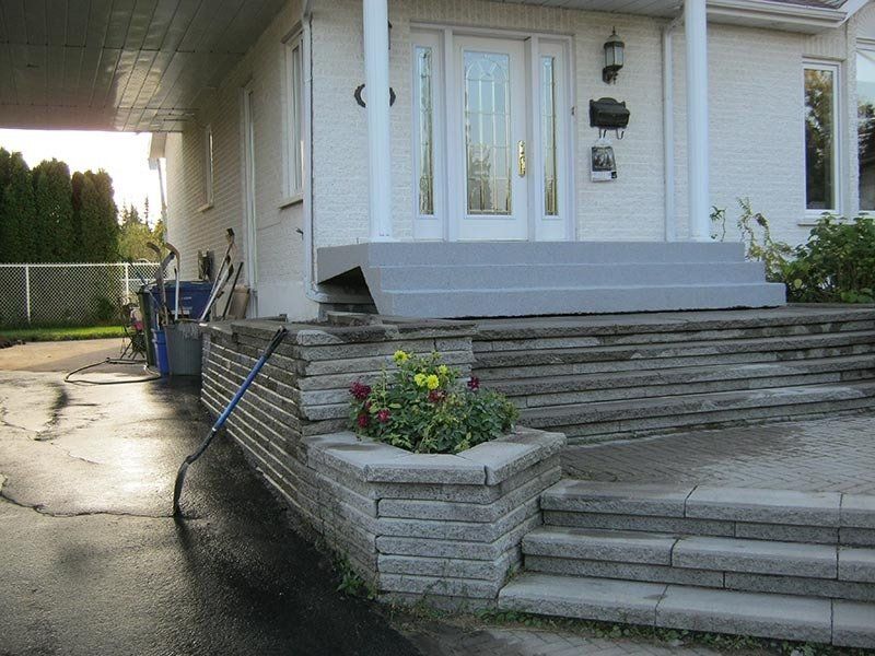 Une maison avec une entrée en pierre et en béton. Un pot de fleurs avec des fleurs colorées et une allée prolongée.