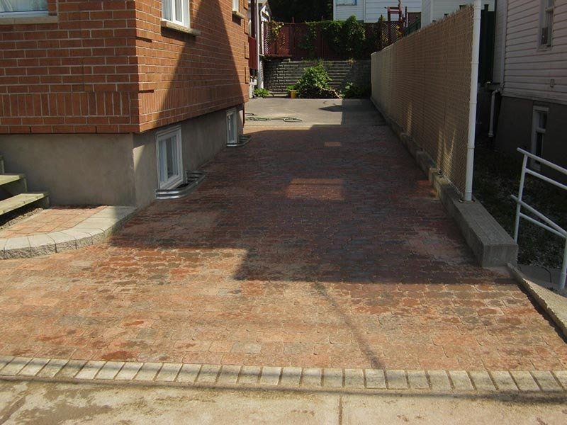 Allée pavée de briques entre le bâtiment en briques et la clôture.