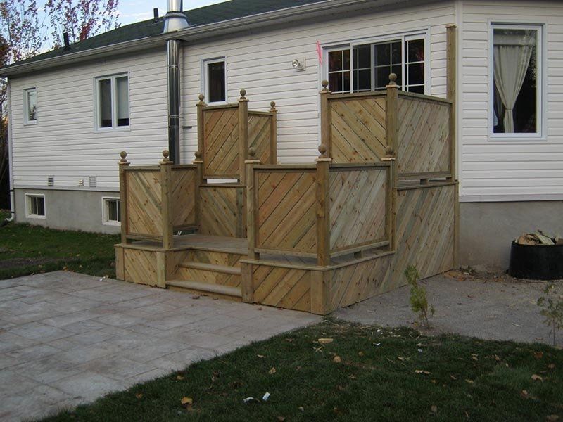 Terrasse en bois avec escalier, adossée à une maison blanche avec patio.