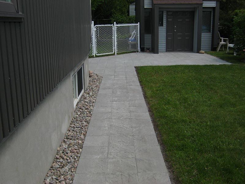 Allée en pierre longeant un bâtiment et de la pelouse, menant à un garage.