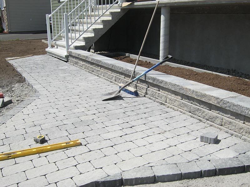 Pose de pavés pour la création d'une terrasse à côté d'un mur de soutènement et d'un escalier.