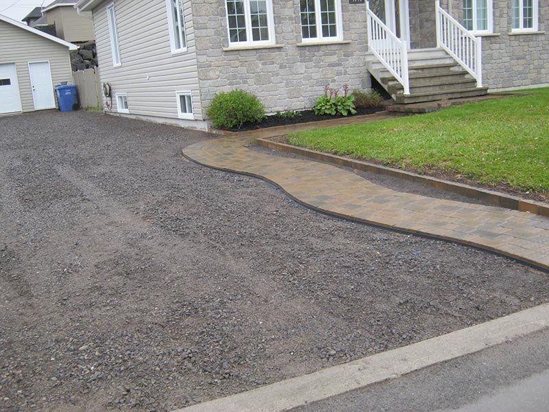 Allée de gravier menant à une maison revêtue de pierre avec allée paysagée et pelouse.