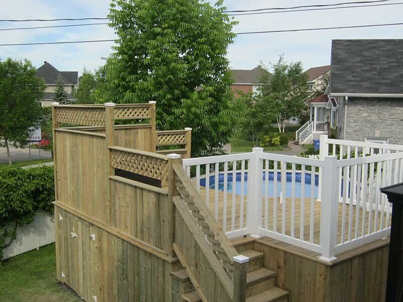 Terrasse en bois avec piscine, escalier et rambarde blanche dans un jardin.