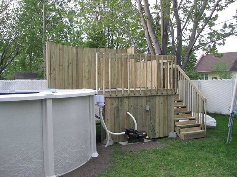 Terrasse en bois avec escalier jouxtant une piscine hors sol ; la pompe de filtration est visible.