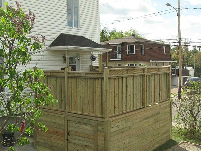 Terrasse en bois avec clôture assurant l'intimité, attenante à une maison blanche à deux étages et donnant sur la rue.