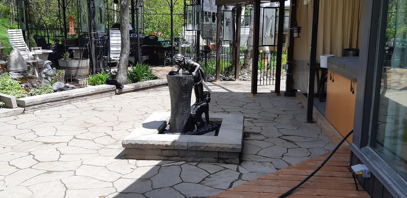 Une sculpture représentant un personnage buvant à une fontaine dans un jardin pavé.