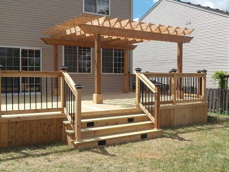 Terrasse en bois avec pergola, escalier, rambarde noire et maison beige en arrière-plan.