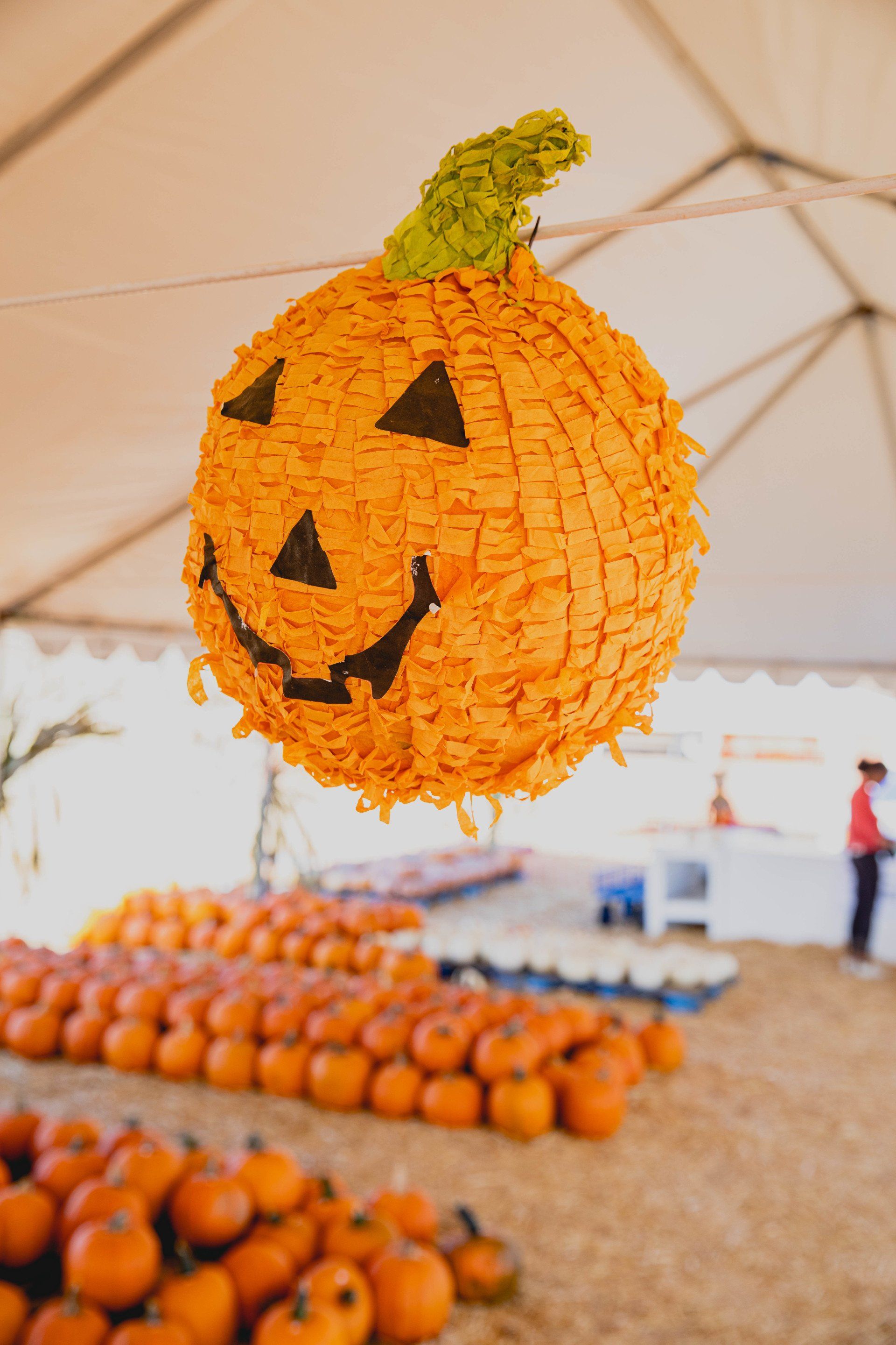 A pumpkin shaped piñata is hanging from a tent