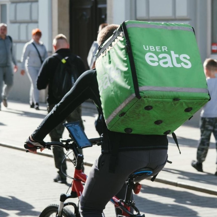 A man riding a bike with a green uber eats bag on his back