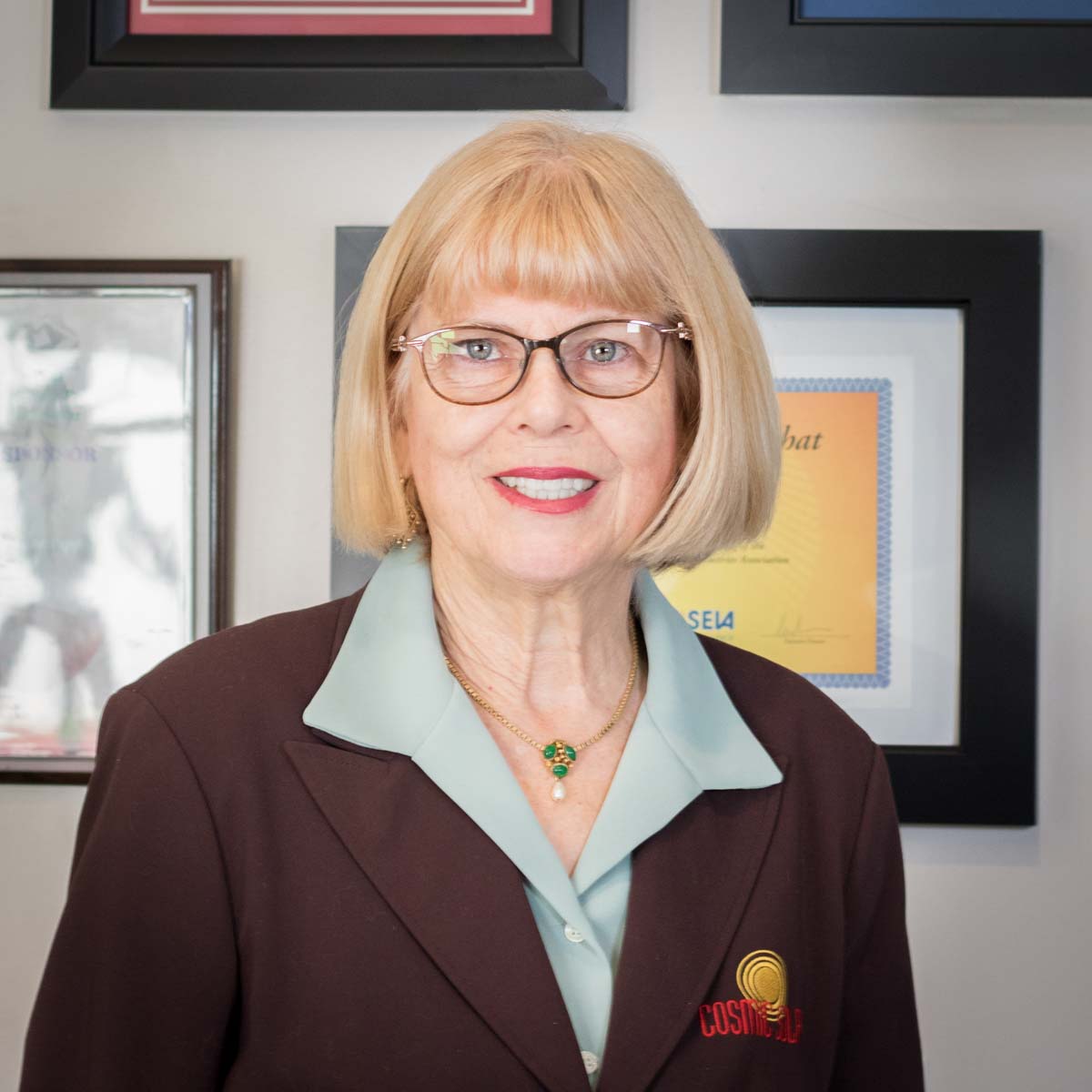 A woman wearing glasses and a brown jacket has a badge on her jacket that says justice