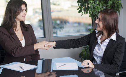 Two ladies at a desk, shaking hands
