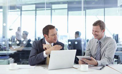 Two men sitting at a laptop computer in an open plan office