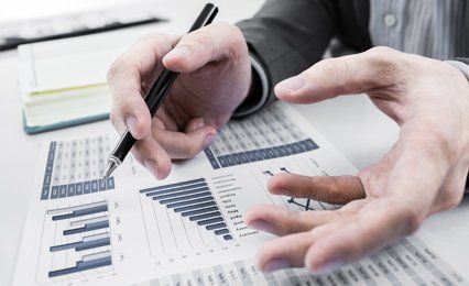 Graphs and charts spread out in front of a man holding a pen