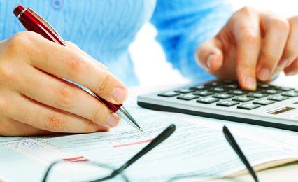 A lady with a pen in one hand, using a calculator with the other