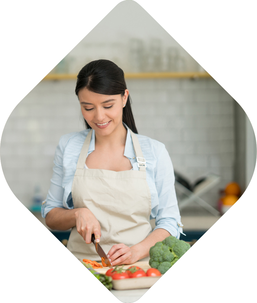 A woman is cutting vegetables on a cutting board in a kitchen.