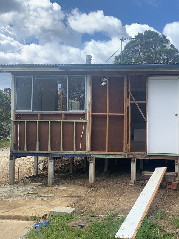 House under construction; exposed wooden frame with windows and door. Exterior is brown, white, and gray.
