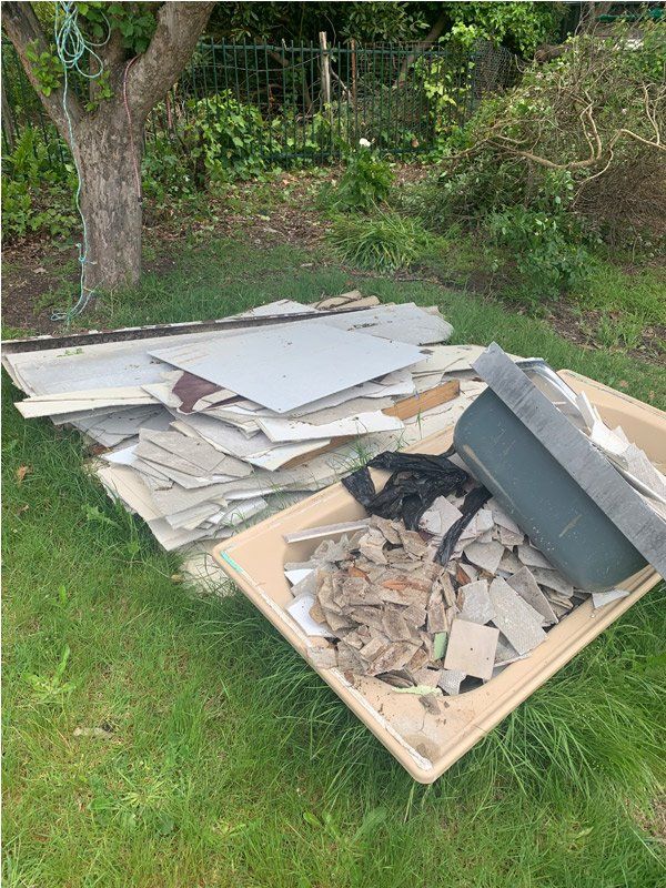Pile of construction debris and a bin of trash on grass. Tree in the background.