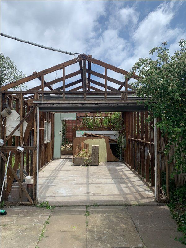 Open-framed, dilapidated garage structure; concrete driveway; visible debris inside; blue sky.