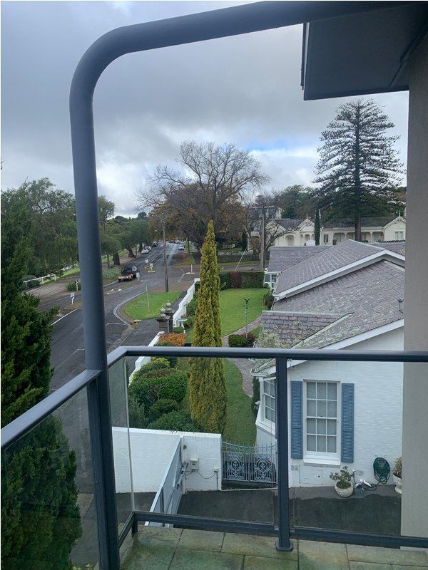 View from a balcony overlooking a street, green lawn, white houses, and cloudy sky.