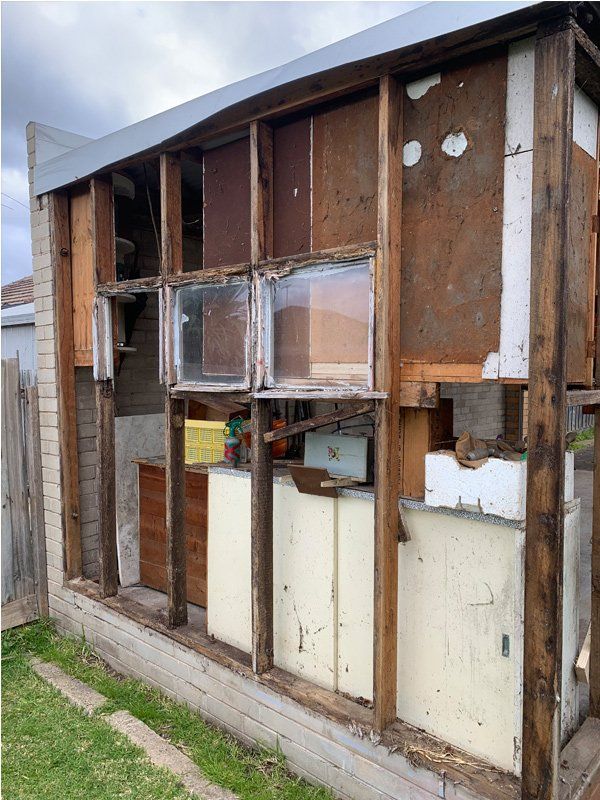 Exterior wall of a building under demolition, showing exposed framing, windows, and debris.