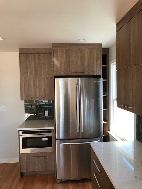Modern kitchen with stainless steel refrigerator, built-in oven, wooden cabinets, and light countertops.