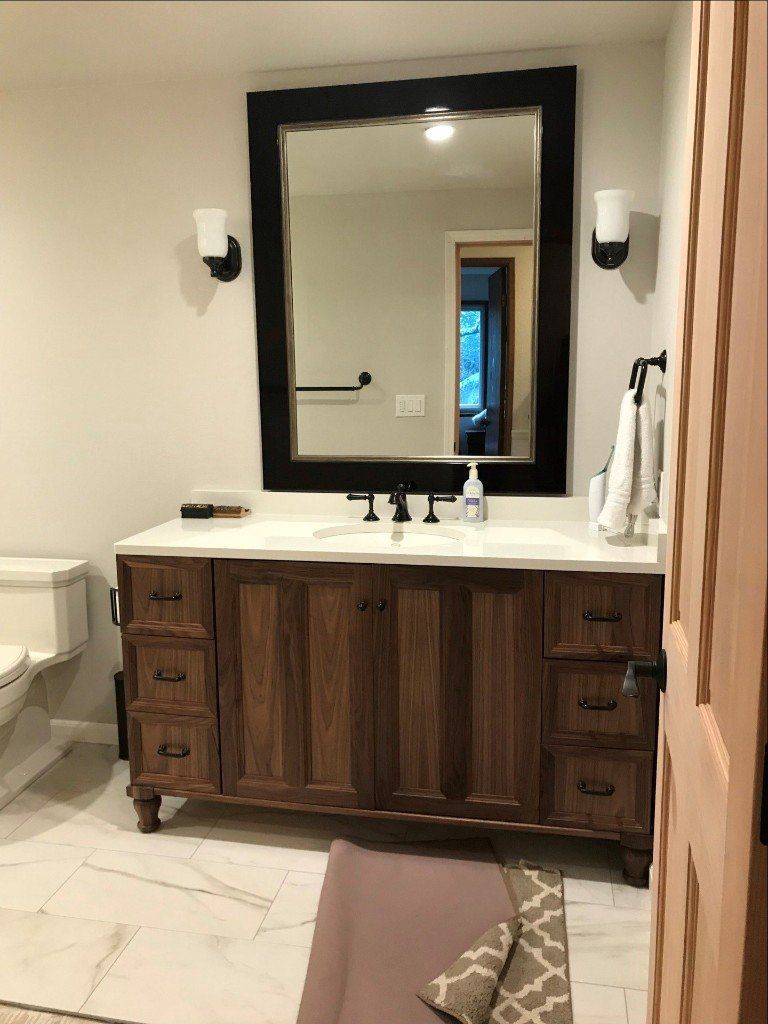 Bathroom vanity with large mirror, white sink, wood cabinet, wall sconces, and beige tile floor