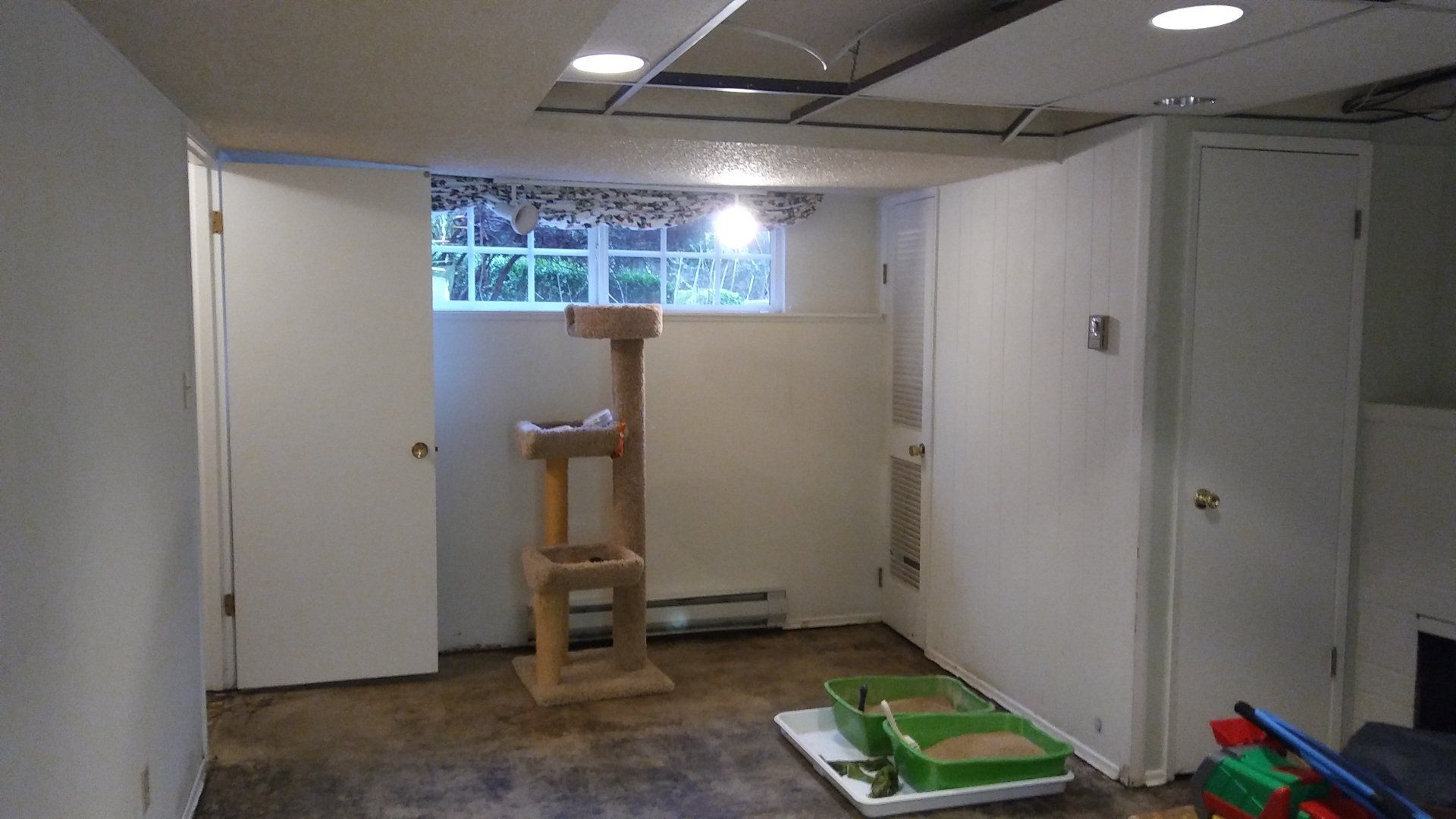 Basement room with white walls, small window, wooden cat tree, and pet items on the floor.