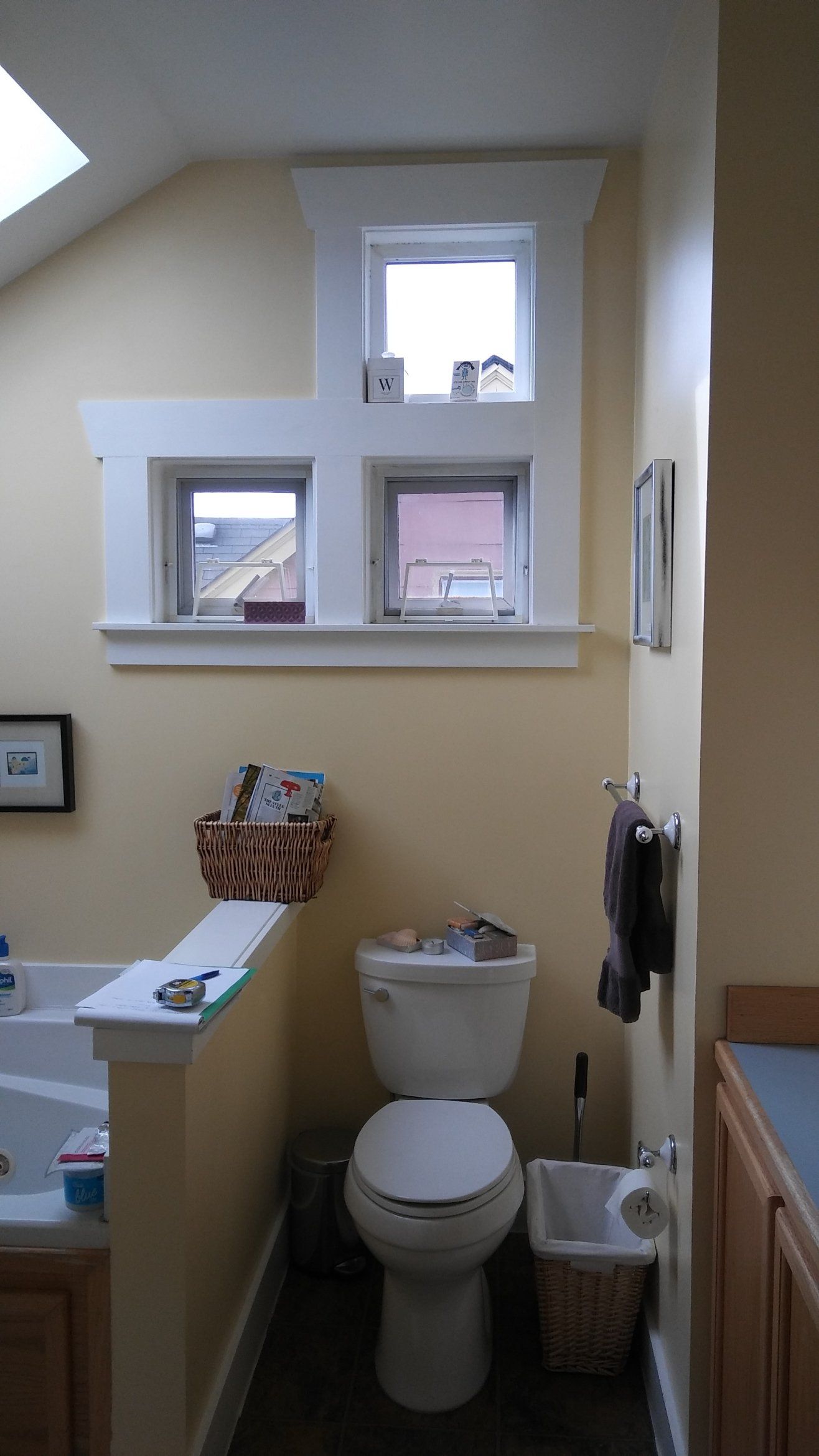 Small beige bathroom with toilet, sink, and two windows above the toilet.