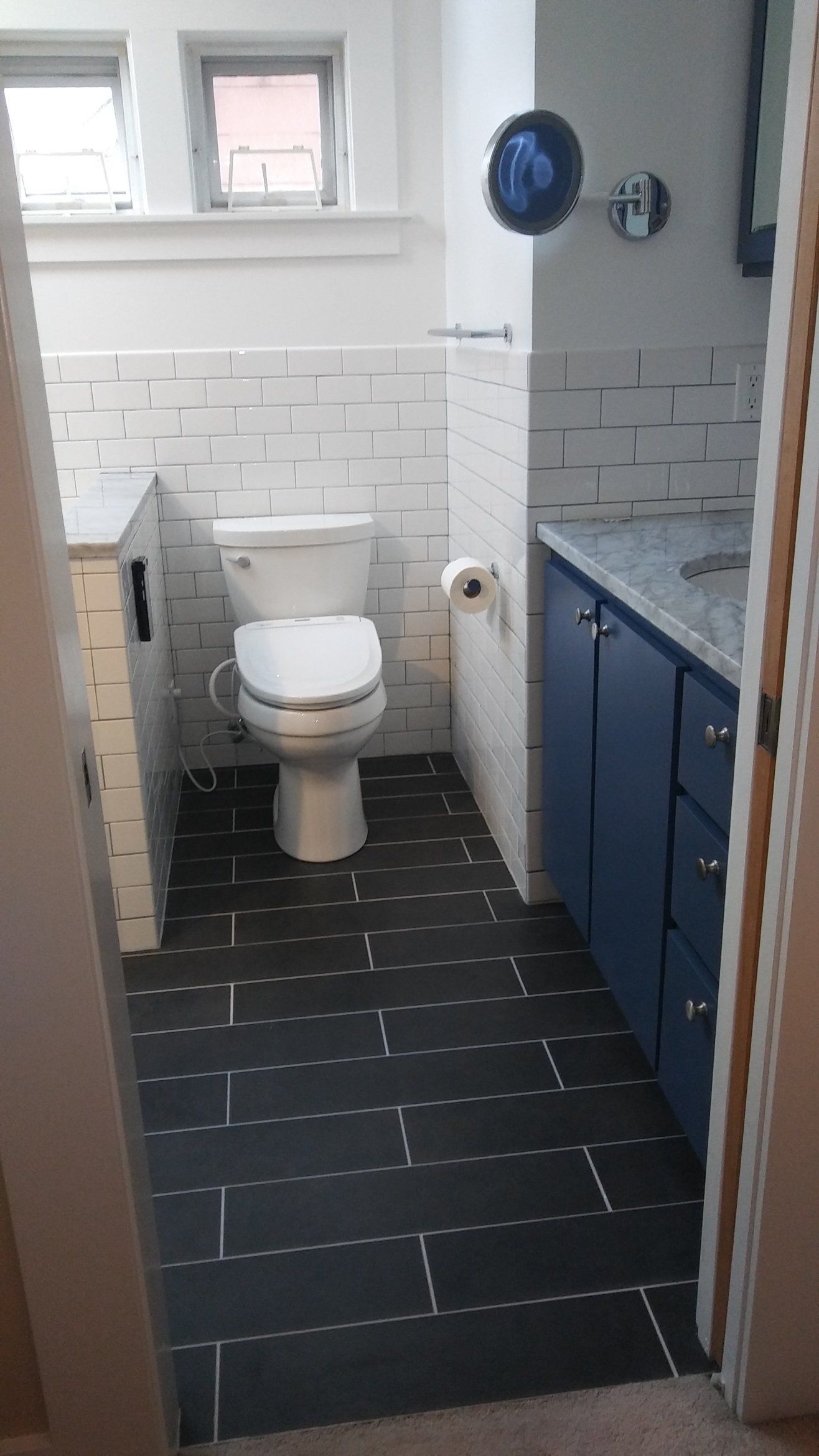 Small bathroom with white toilet, dark tiled floor, and blue vanity cabinets.