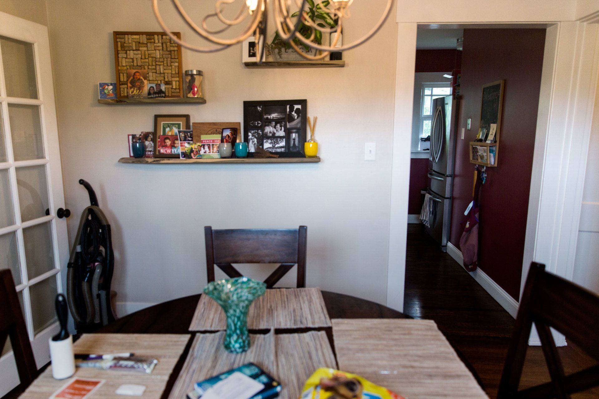 Dining room with a table, chairs, wall shelf decor, and a doorway to a hallway and kitchen.