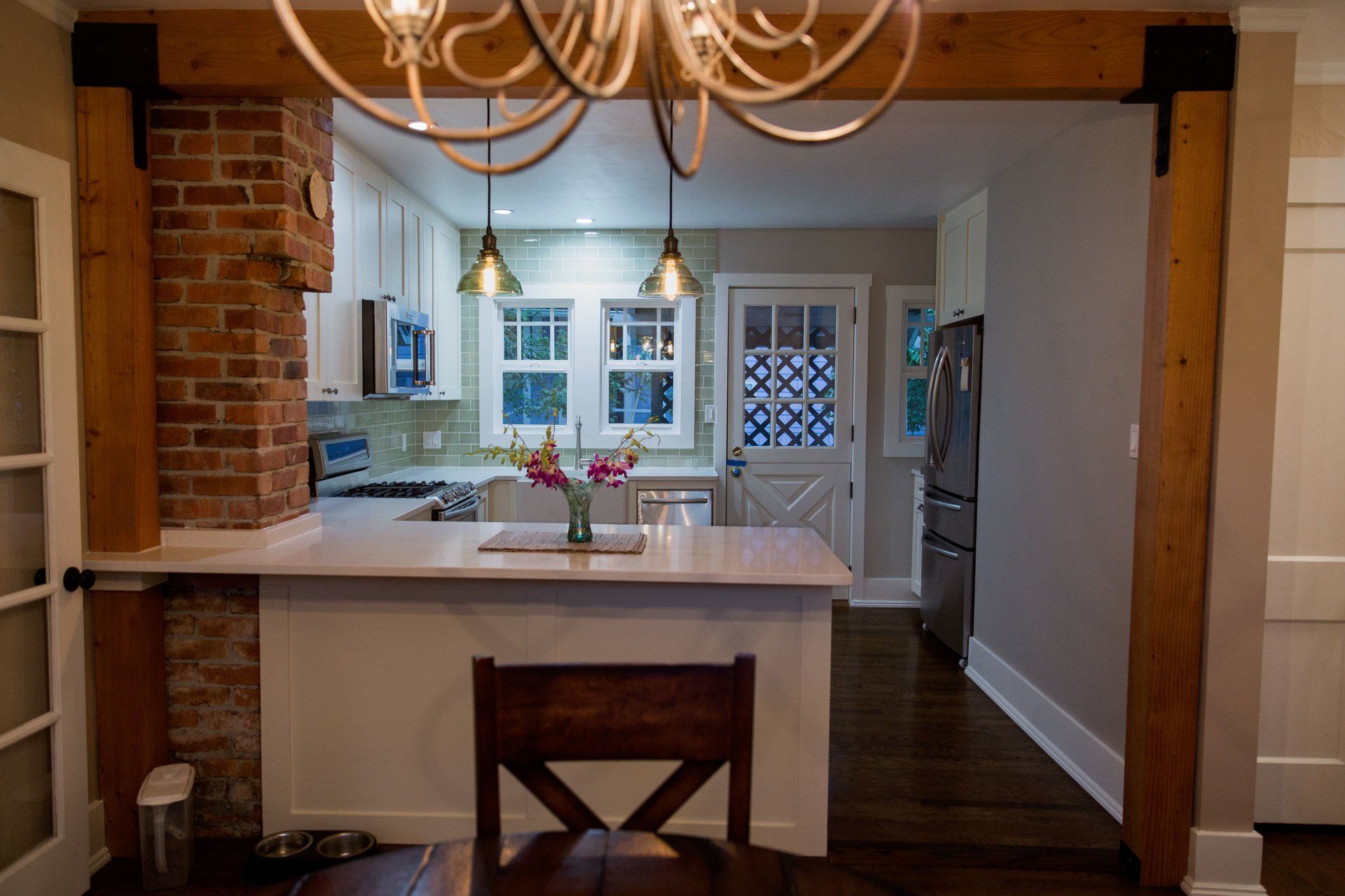 Kitchen view through a dining room with a white island, wood beams, and chandelier lighting.