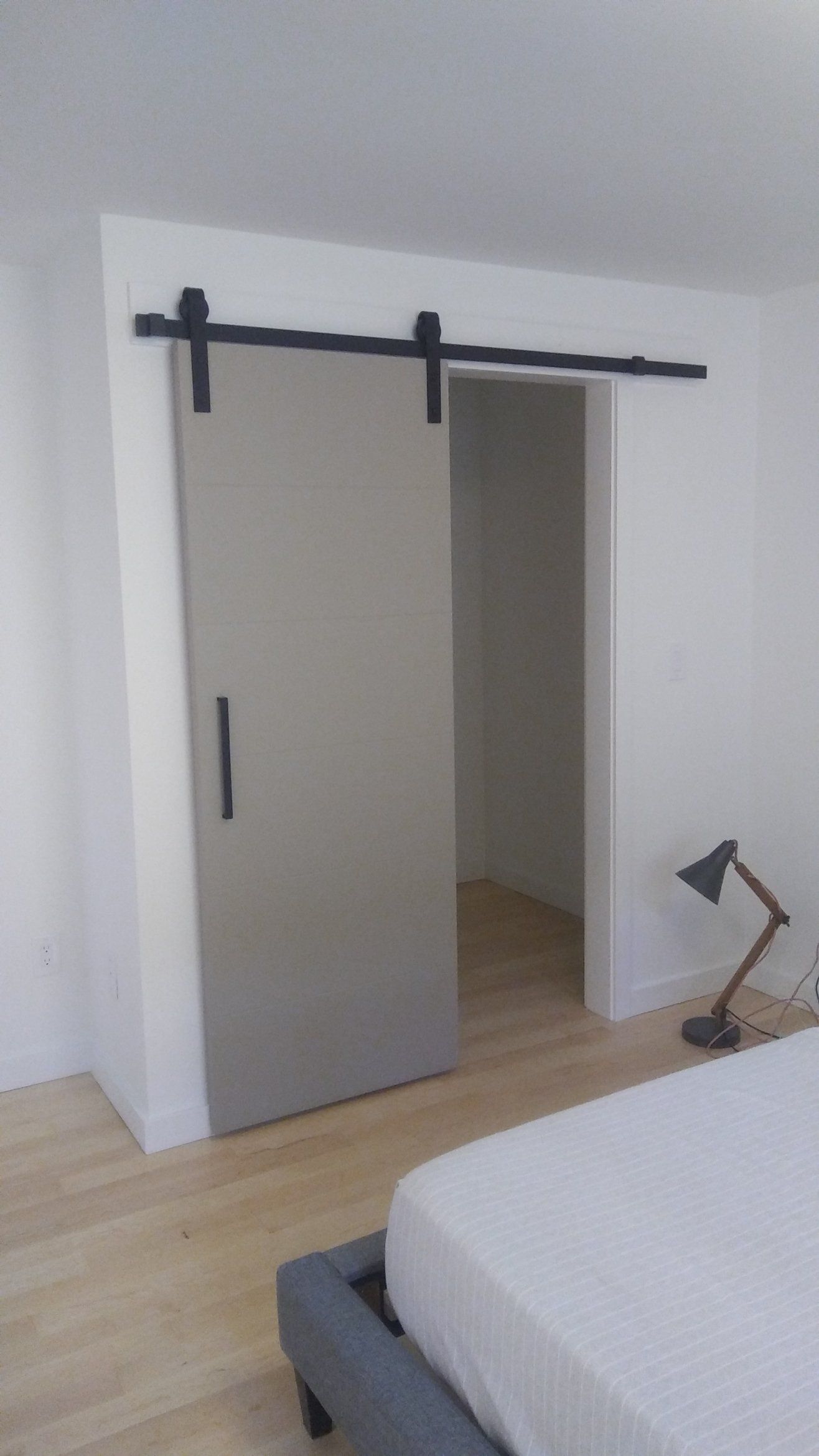 Modern bedroom with a sliding closet door open, showing an empty doorway and a bedside lamp.