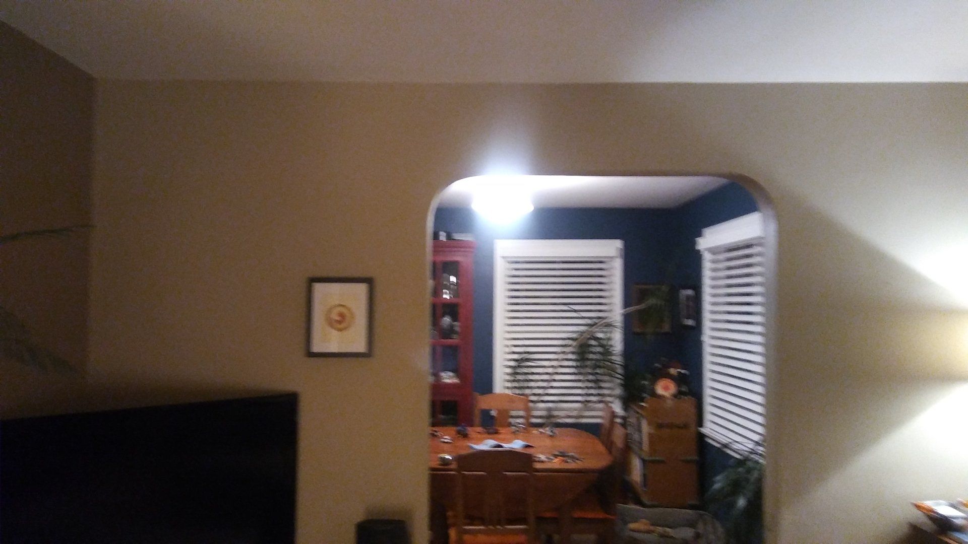 Living room view into a dining area with a bright light, wooden table, chairs, and a window with blinds