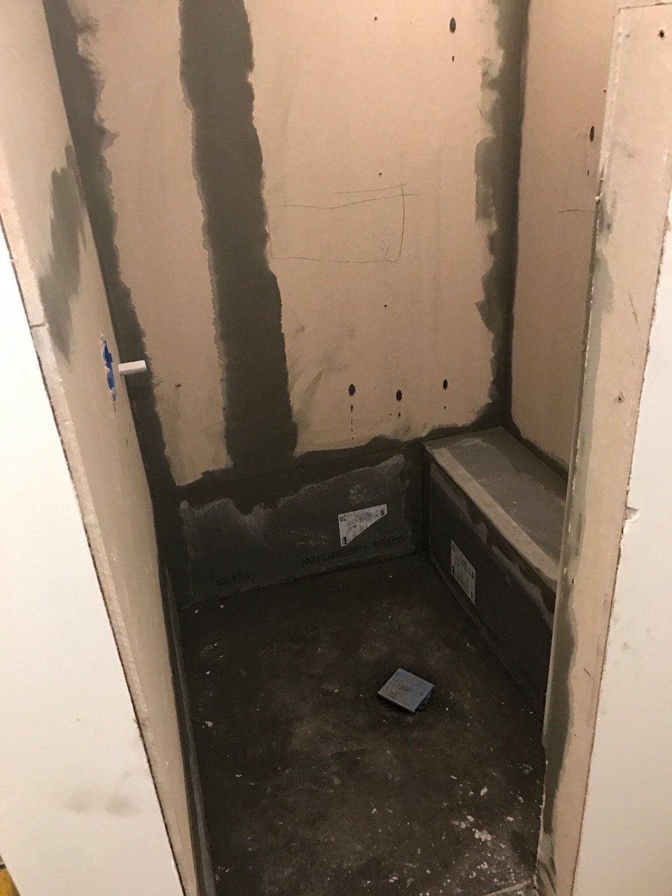 Small unfinished shower or utility alcove with dark floor, exposed walls, and debris on the ground.