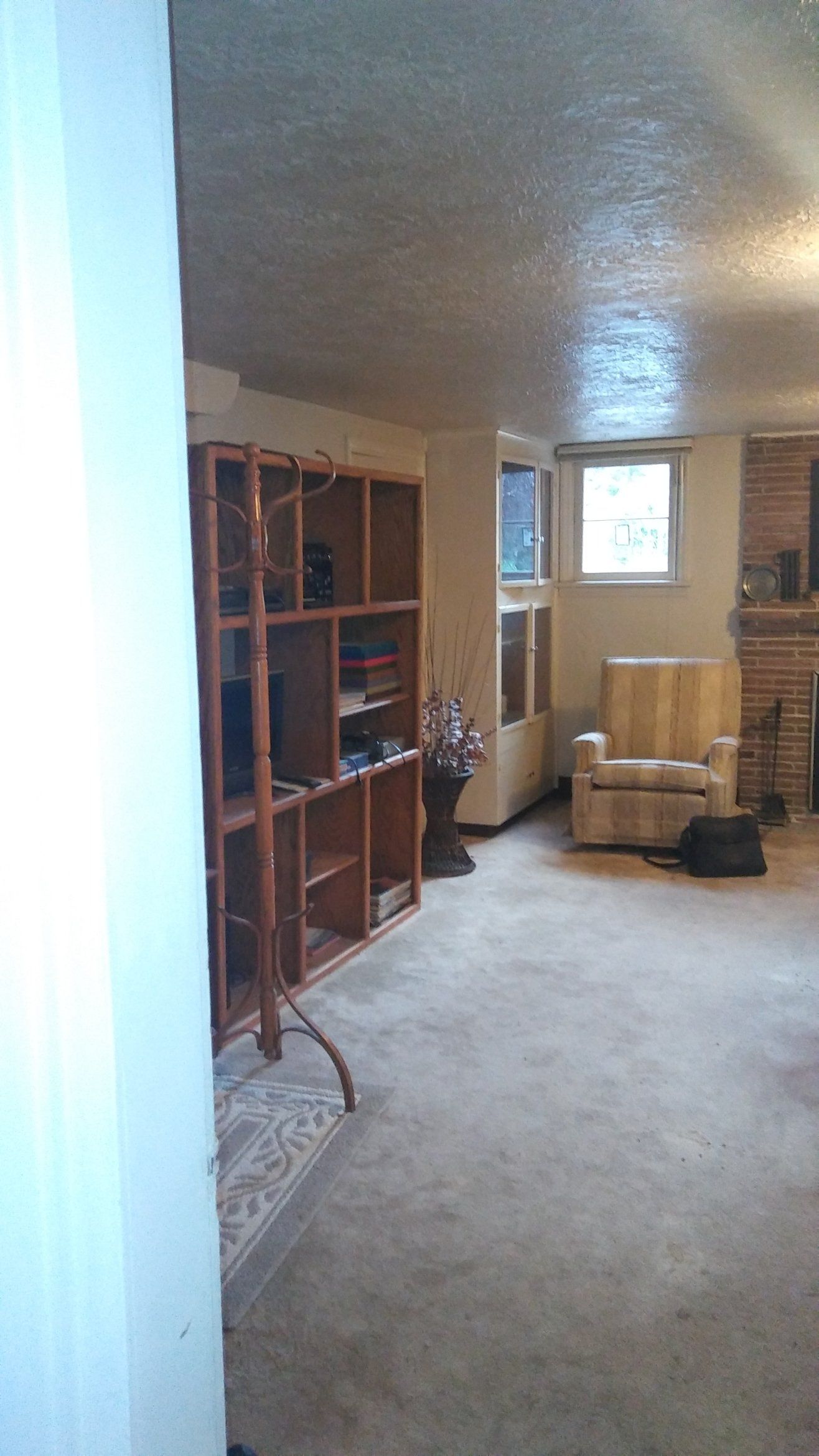 Cozy living room with beige carpet, wooden shelves, armchair, lamp, and window in the back.