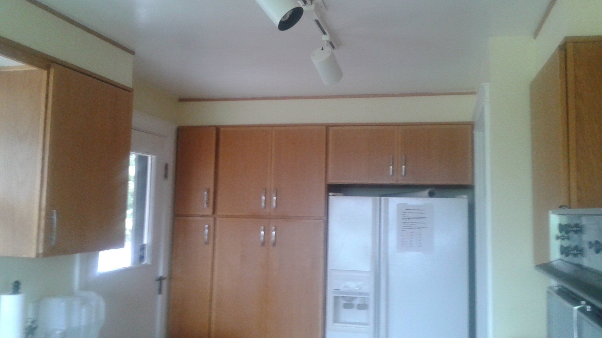Kitchen with wooden cabinets, white ceiling track lights, and a white refrigerator beside a counter.