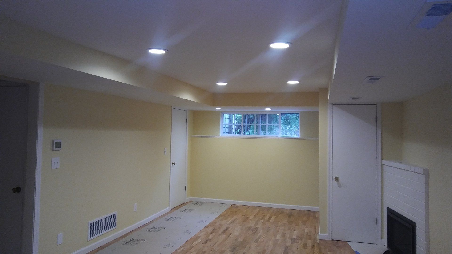 Empty basement room with recessed lights, wood floor, and a small window.