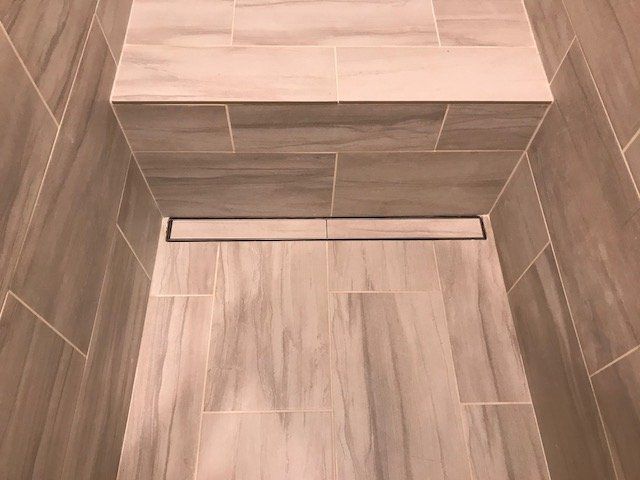 Brown tiled bathroom floor with a rectangular shower drain and raised step.