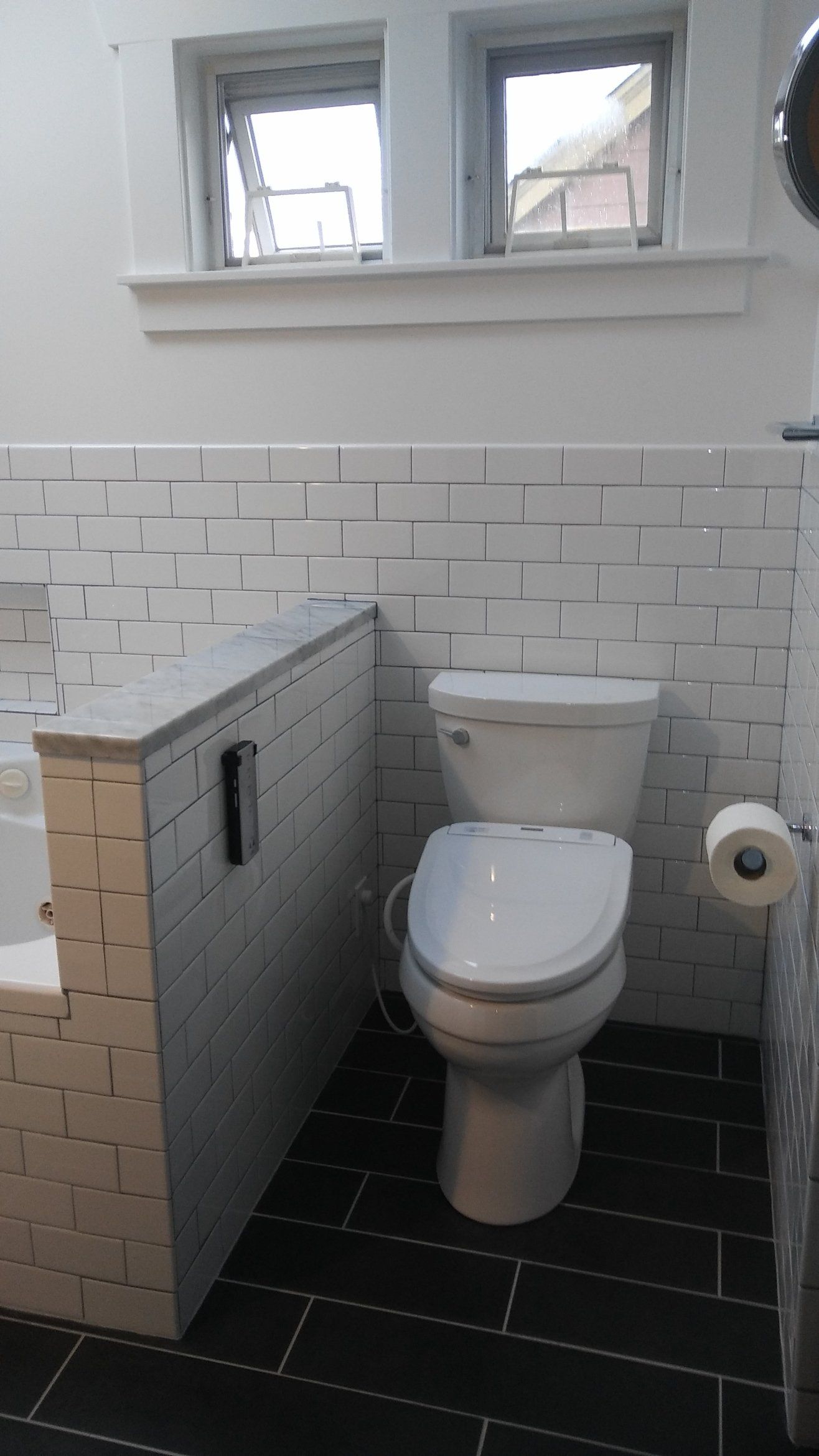 Accessible restroom with a white toilet, tiled walls, and a side privacy partition under small windows