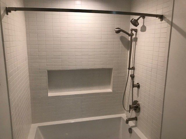 White tiled shower with built-in niche and handheld showerhead with grab bar set.