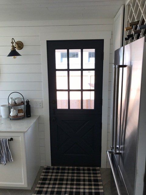Black front door with window, plaid rug, and white kitchen cabinets in a narrow entryway
